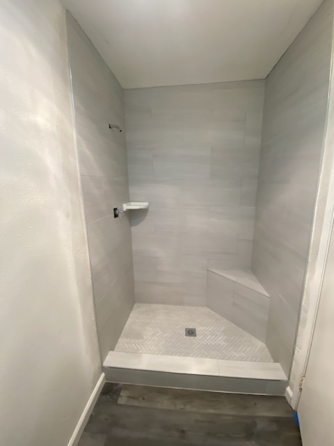 Modern walk-in shower with light gray tile walls, built-in corner bench, and tiled shower floor.