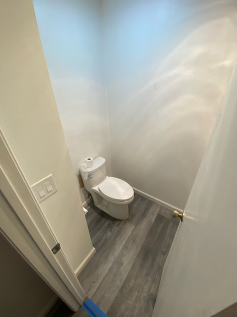 Minimalist toilet installation in separate water closet with gray plank flooring and white walls.