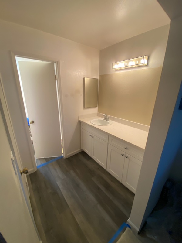 Updated bathroom vanity with white shaker cabinets, quartz countertop, and wall-mounted mirror under modern light fixture.