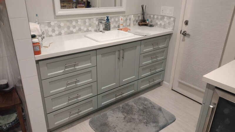 Bathroom remodel with single-sink vanity, gray shaker-style cabinets, quartz countertop, and updated tile backsplash.