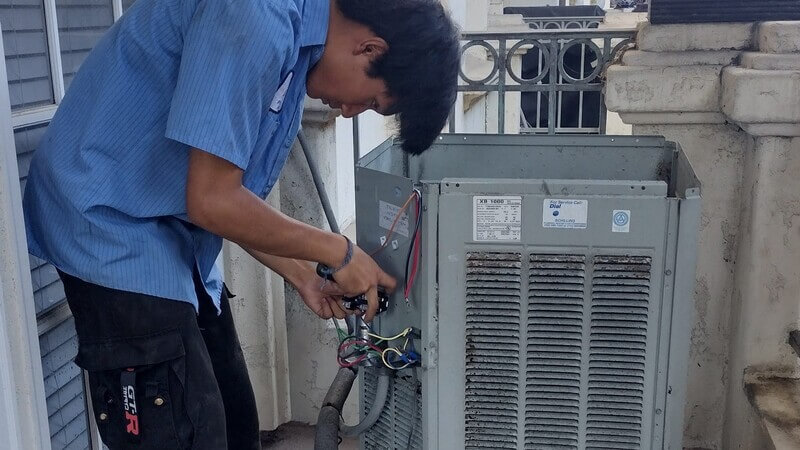 Dial ONE technician repairing electrical components on outdoor air conditioning unit during residential AC service call.