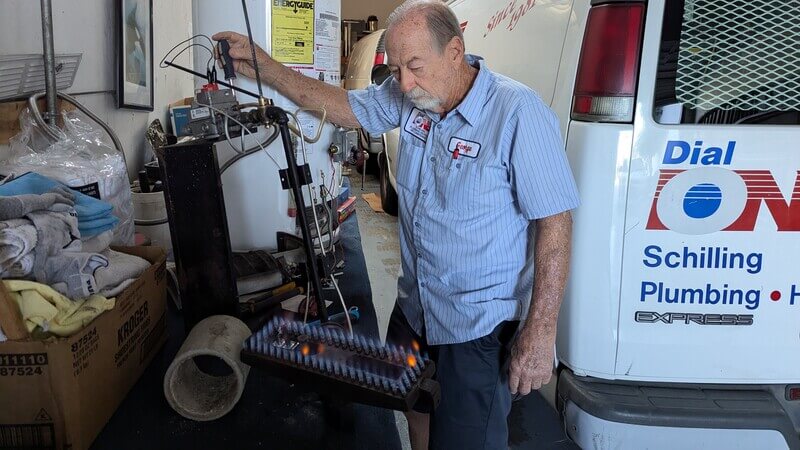 George Schilling technician testing gas furnace burner assembly during heating system repair in service garage.
