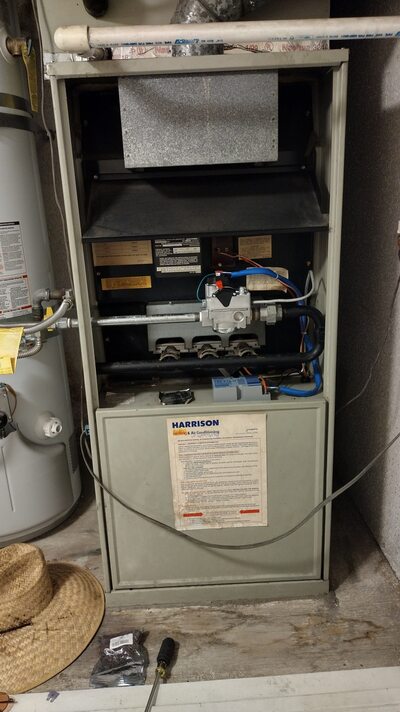 Open upright gas furnace unit with exposed burners and control wiring, located in residential utility space.
