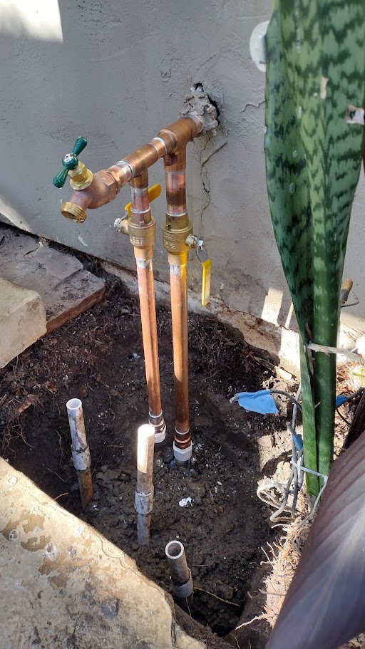Dual hose bib installation with green handles, copper piping, and two ball shutoff valves, prepared for irrigation and outdoor water access.