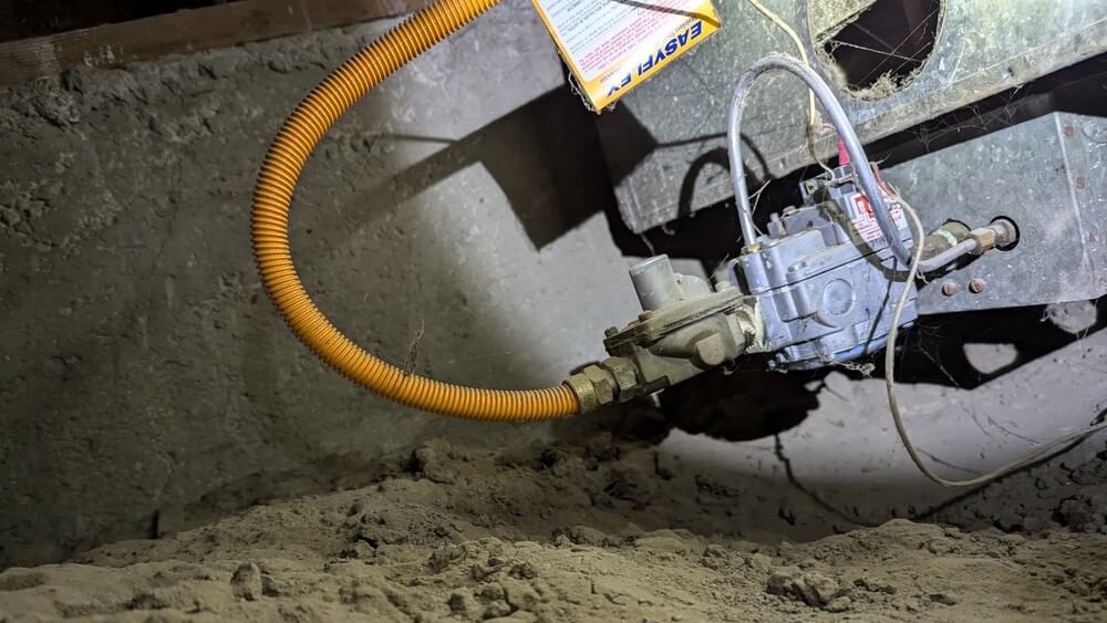 Gas furnace valve and flexible gas line in crawl space during heating system repair.