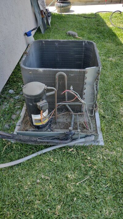 Disassembled outdoor AC condenser unit showing exposed compressor and coil.