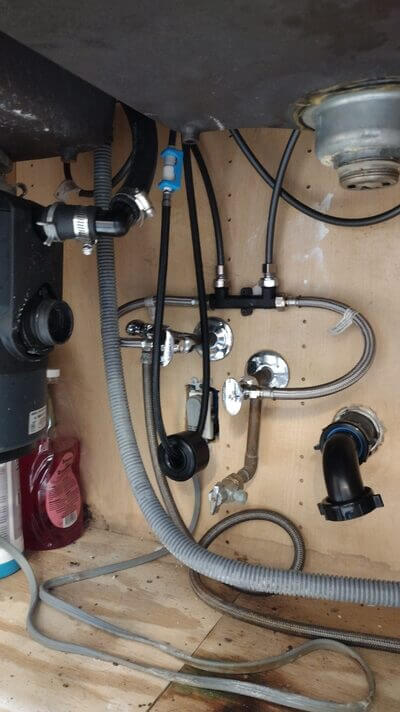 Newly installed water supply lines, valves, and drainage under kitchen sink.