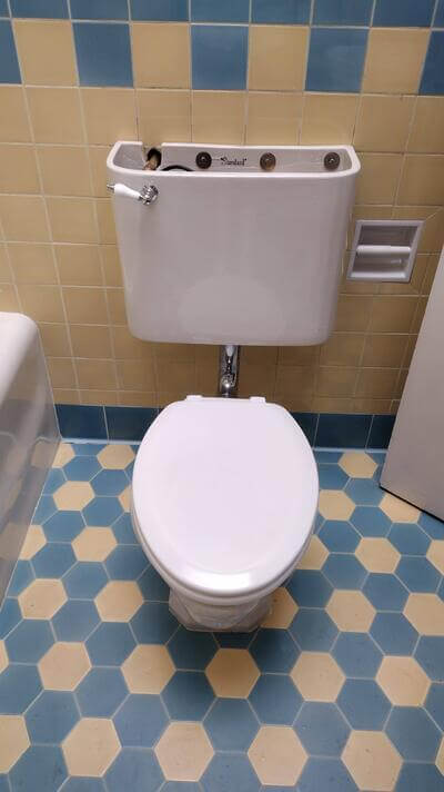 New toilet installation with exposed tank hardware in tiled Long Beach bathroom.