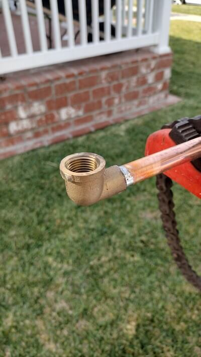 Close-up of soldered copper pipe with brass elbow fitting.