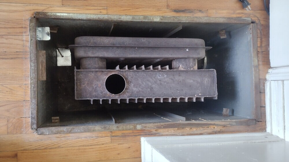 Interior view of an old radiant ceiling heater box showing rust and corrosion on heat exchanger.