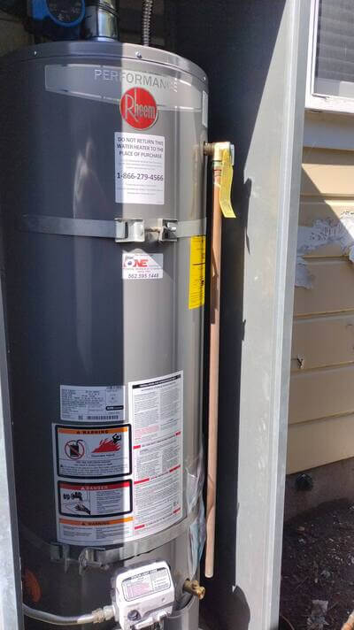 Rheem water heater installed outdoors with visible service sticker from Dial ONE Schilling.