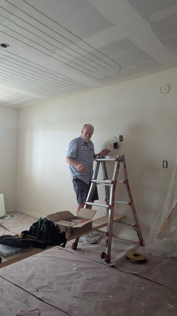 Dial ONE Schilling technician working on electric radiant ceiling heat repair in a residential room, standing beside ladder and tools.