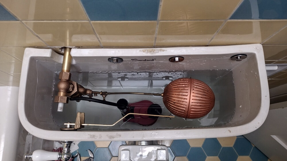 Inside view of an older toilet tank showing plumbing components and repair work in a Lakewood home.