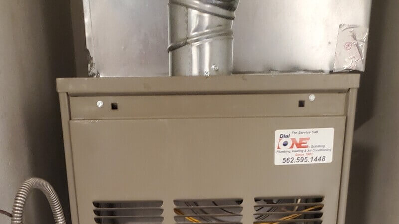Gas furnace unit with Dial ONE Schilling service label during furnace repair in Lakewood, CA.
