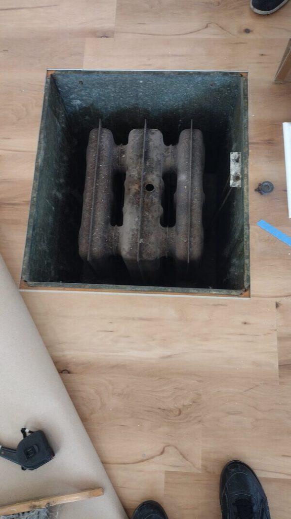 Vintage gas floor furnace with exposed cast-iron heating core set in hardwood flooring during maintenance in a Lakewood, California residence.